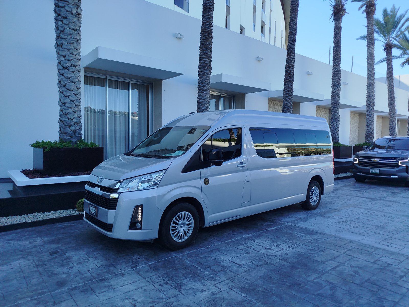 Toyota Hiace plateada de Torote Luxury Transportation frente a un edificio en Los Cabos.
