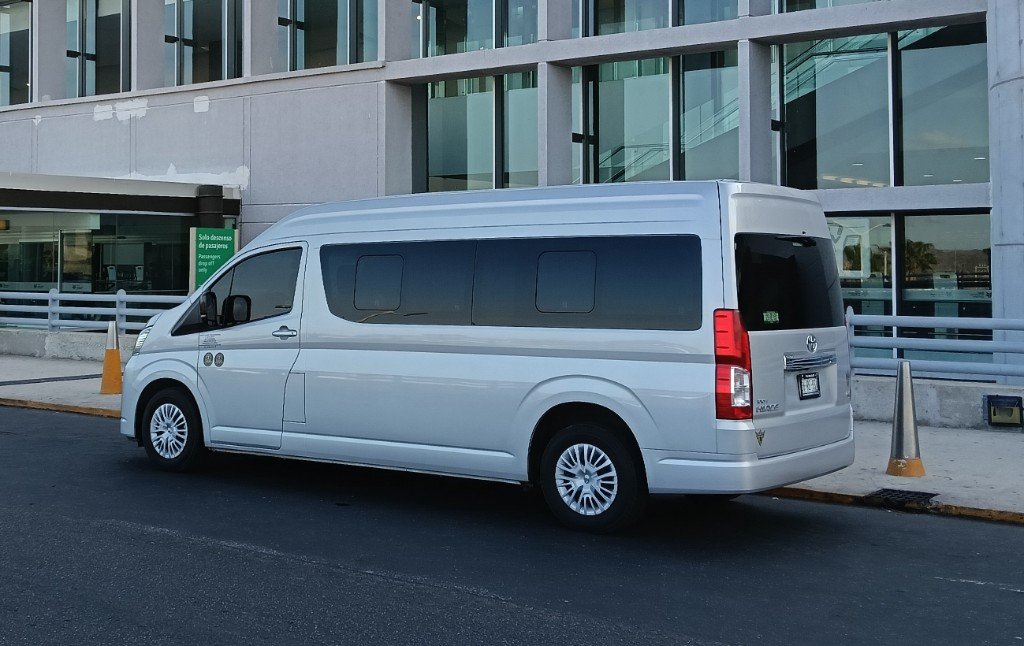 Toyota Hiace plateada de Torote Luxury Transportation en zona de descenso de pasajeros.
